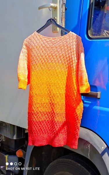 Orange‑roter gestrickter Longpullover mit 3/4-Ärmeln an einem Kleiderbügel
