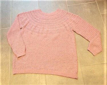 Altrosa gehäkelter Damenpullover auf Fliesenboden, von oben fotografiert.