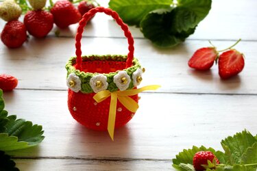 Small crocheted strawberry-shaped basket with braided handle, green rim and white flower appliqu
e s