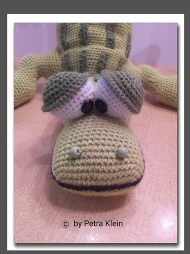 Nahaufnahme eines gehäkelten Amigurumi-Krokodils in Hell- und Dunkelgrün mit großen Augen und sichtbarer Maschenstruktur.