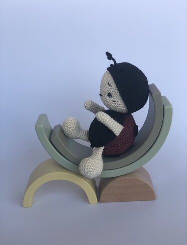 gehäkeltes Amigurumi-Marienkäfer-Püppchen auf gestapelten Holzbögen