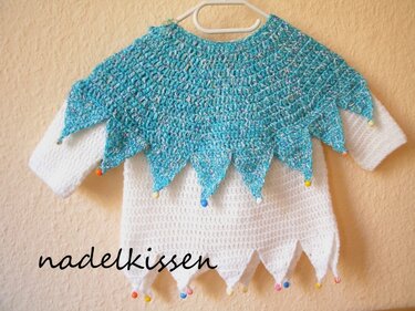 Gehäkeltes Kinderkostüm: weißer Pullover mit türkisem Zipfelponcho und bunten Perlen an den Zipfelspitzen
