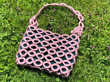Gehäkelte Henkeltasche in Rosa und Dunkelgrün mit Ringmuster auf Gras