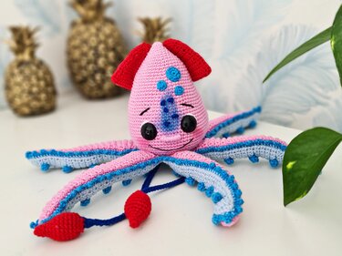 Gehäkelter pink-blauer Amigurumi-Tintenfisch mit schwarzen Augen und bunten Tentakeln