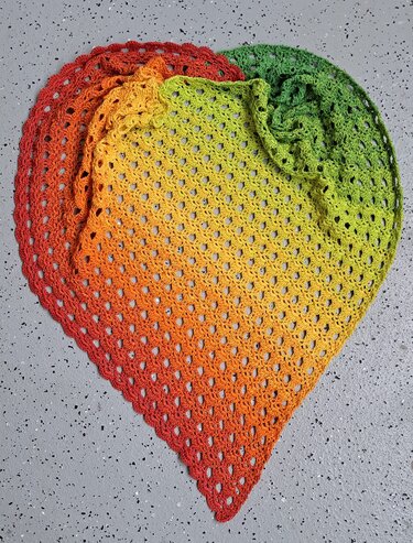 Gehäkeltes dreieckiges Tuch mit Verlaufsgarn in Grün, Gelb, Orange und Rot auf grauem Untergrund
