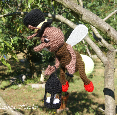 Gehäkeltes Amigurumi-Glühwürmchen mit Zylinderhut und Laterne, aufgehängt an einem Ast