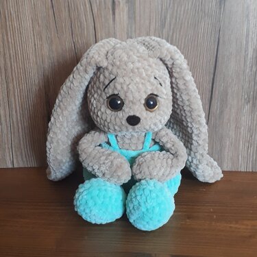 Gehäkelter Amigurumi-Hase in Beige mit langen Ohren und türkisfarbener Latzhose, sitzend