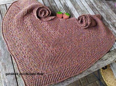 Nahaufnahme eines gehäkelten Dreieckstuchs mit Strukturmuster in melierten Rosa- und Brauntönen auf Holzuntergrund