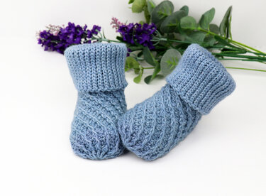 Light blue knitted baby booties with folded ribbed cuffs and diagonal textured stitch.