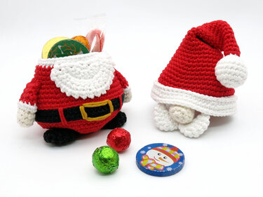 Red crocheted Santa candy holder with belt filled with foil chocolates next to a red and white crocheted Santa hat