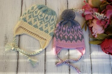 Two knitted baby earflap hats, blue-cream and pink-gray, with braided ties