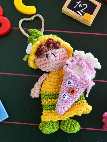 Gehäkelter Schlüsselanhänger Schulmädchen mit braunen Haaren, gelb-grünem Kleid, rosa Schultüte mit ABC-Perlen und herzförmigem Metallring