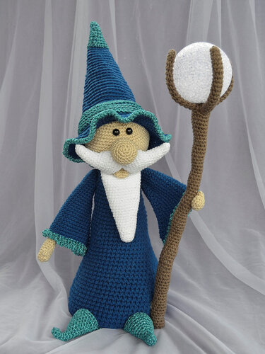 Gehäkelte Amigurumi-Zauberer-Puppe in blauem Gewand mit weißem Bart und Zauberstab mit weißer Kugel