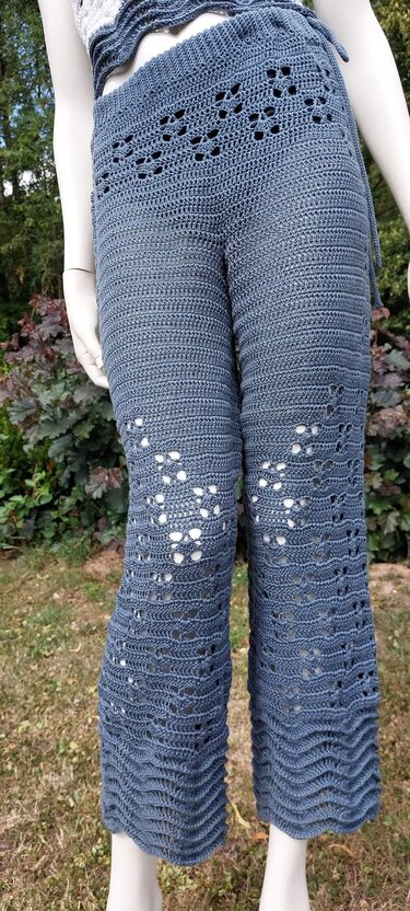 Blaue gehäkelte Damenhose mit filigranem Lochmuster und wellenförmigem Saum an einem Mannequin