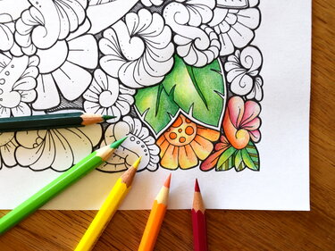 Teilweise kolorierte Ausmalvorlage mit Blumen- und Blattmuster und fünf liegenden Buntstiften