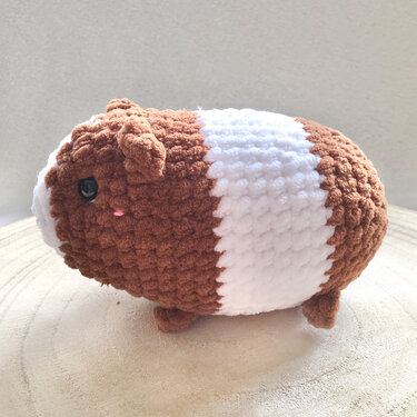 Gehäkeltes Meerschweinchen-Amigurumi in Braun und Weiß auf Holzuntergrund