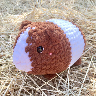 Brown and white crocheted guinea pig amigurumi sitting on straw