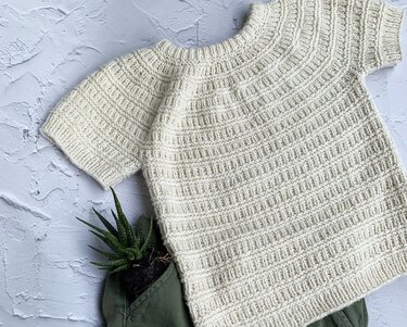 Nahaufnahme eines kurzärmligen Kinderpullovers in Creme mit deutlicher Rippenstruktur