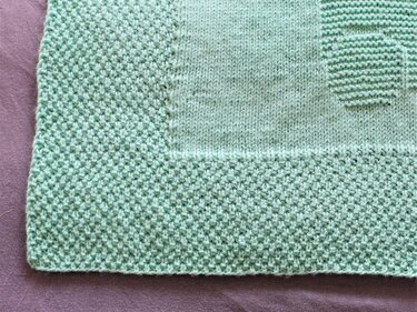 Close-up of mint knitted baby blanket showing textured border and smooth center