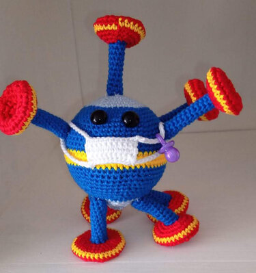 Gehäkelte blaue Amigurumi-Kugel mit mehreren Armen, roten Scheibenfüßen, weißer Maske und violettem Schnuller