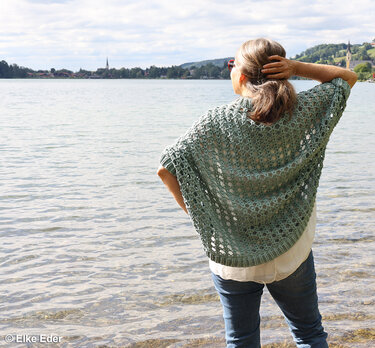 Back view of a woman wearing a sage green openwork crocheted shrug by a lake