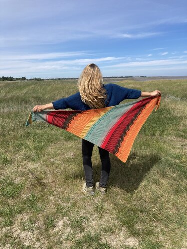 Person von hinten hält mehrfarbiges gestricktes Dreieckstuch mit Streifen und Zierreihen