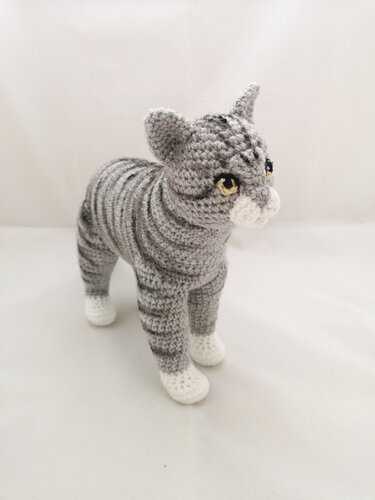 Gehäkelte graue gestreifte Amigurumi-Katze mit weißen Pfoten
