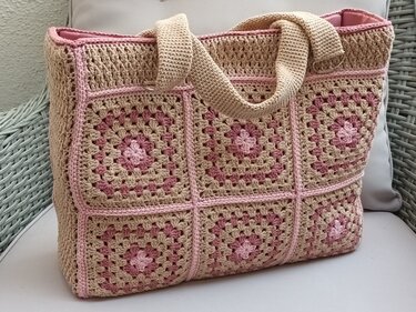 Nahaufnahme einer gehäkelten Henkeltasche aus beigen und rosa Granny‑Squares mit gehäkelten Henkeln