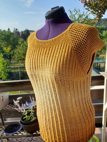 Senfgelbe, handgehäkelte Damen-Tunika mit Rippen- und Lochmuster auf einer Schneiderpuppe im Freien.