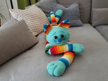 Gehäkelte bunte Katze aus gestreiftem Garn auf grauem Sofa mit Kissen