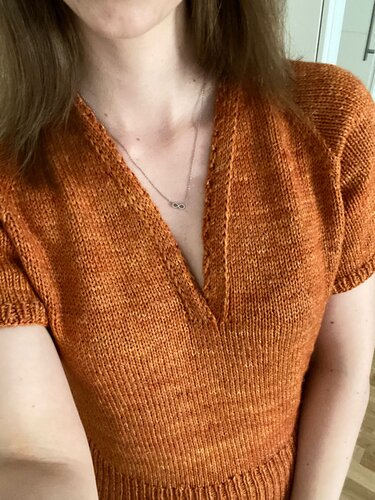 Close-up of rust-colored short-sleeve V-neck sweater showing stockinette stitch and ribbed hem