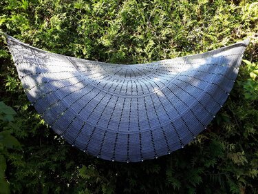 Gehäkeltes Halbrundtuch in Grau mit Farbverlauf, Lochmuster und Perlen vor grünem Hintergrund