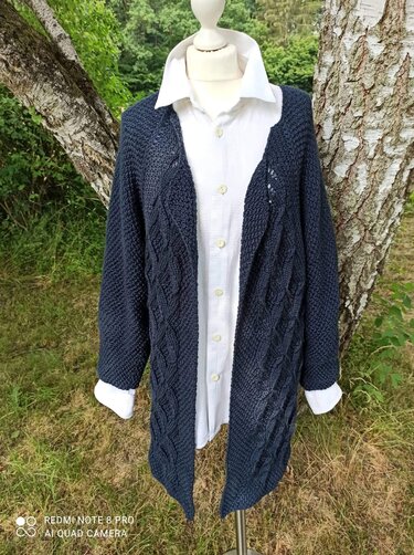 Dunkelblaue offene Strickjacke mit Zopfmuster auf Schaufensterpuppe über weißer Bluse vor Baum