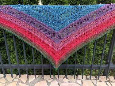 Gehäkeltes Dreieckstuch in Blau, Violett, Pink und Grün mit Lochmuster, über Metallzaun drapiert
