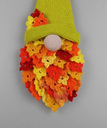 Crocheted gnome wall hanging with green hat and layered autumn floral beard