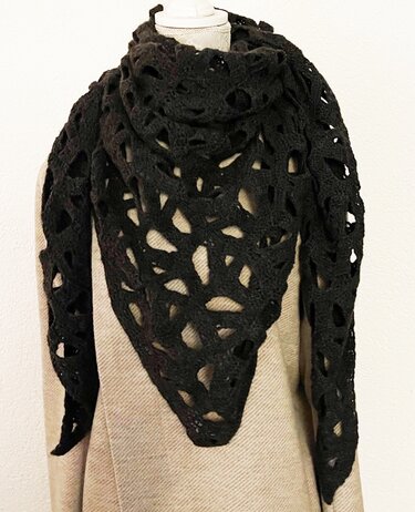 Black crocheted triangle shawl with openwork draped over a beige coat on a mannequin