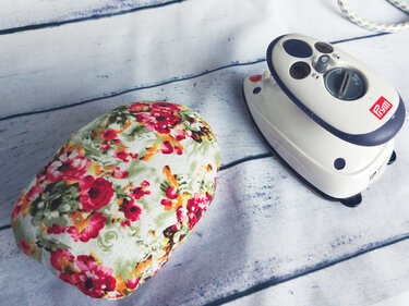 Geblümtes Bügelkissen neben kleinem Bügeleisen auf hellem Holzuntergrund