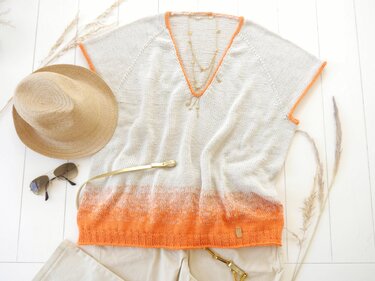 Gestricktes Damen-Shirt mit V-Ausschnitt, kurzen Ärmeln und Ombré-Verlauf von Beige zu Orange, flach liegend mit Strohhut und Sonnenbrille.