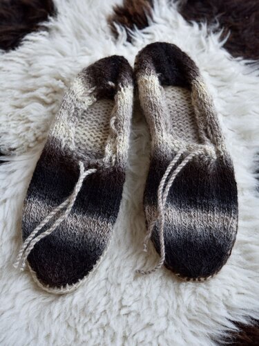 Flache gestrickte Damen-Hausschuhe mit Zierkordel und Farbverlauf auf hellem Fell