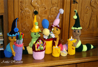 Bunte gehäkelte Amigurumi-Raupen mit Zipfelmützen, Stiftehalter, Körbchen, Blumenvasen und Kerzenhaltern.