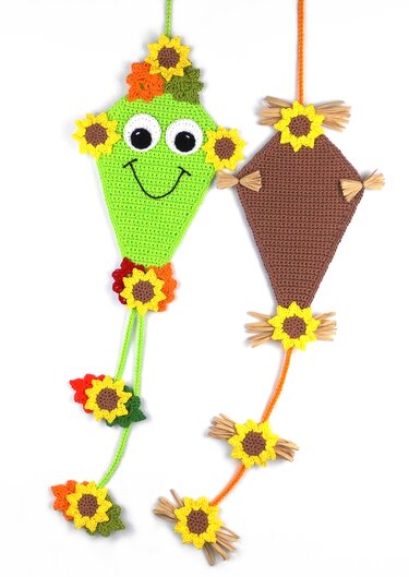 Two crochet kite wall hangings with sunflower appliqués; one green smiling kite and one brown patterned kite with straw tassels