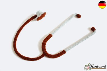 Gehäkeltes Stethoskop-Spielzeug aus braunem und hellgrauem Garn auf weißem Hintergrund