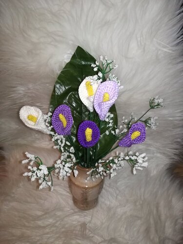 Vase mit gehäkelten Calla-Lilien in Weiß, Flieder und Lila, gelber Kolben, großes grünes Blatt und weiße Beiwerkzweige auf hellem Felluntergrund