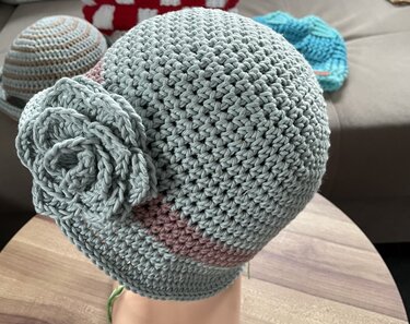 Gehäkelte mintgrüne Damenmütze mit seitlicher Blüte und rosa Streifen auf Kopfmodell