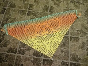 Handgehäkeltes Dreieckstuch mit Ombre-Farbverlauf (Türkis–Orange–Gelb), stilisiertem Katzenmotiv im Filethäkelmuster und kleinem Metallanhänger.