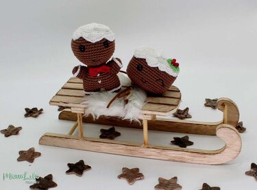 Gehäkelter Lebkuchenmann und Weihnachtspudding auf einem Holzschlitten mit Sternen