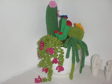 Weißer Blumentopf mit gehäkelten Pflanzen: Säule, Kugel und hängende Ranken in Grün mit pinken Akzenten