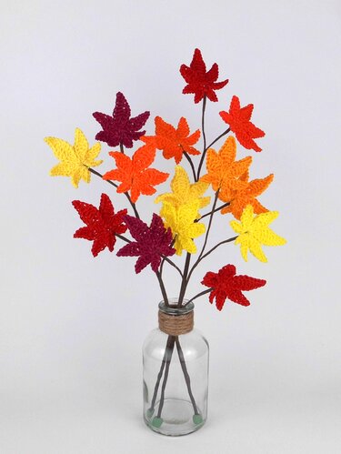 Glasvase mit Stielen und gehäkelten Herbstblättern in Gelb, Orange, Rot und Dunkelrot