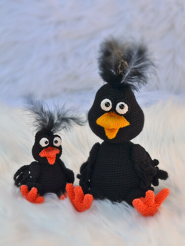Große und kleine gehäkelte Amigurumi-Krähe nebeneinander, schwarze Körper, orange Schnäbel und Füße mit Federkamm