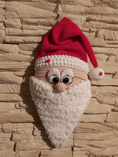 Gehäkelter Weihnachtsmannkopf mit roter Mütze und weißem Bart an Steinwand